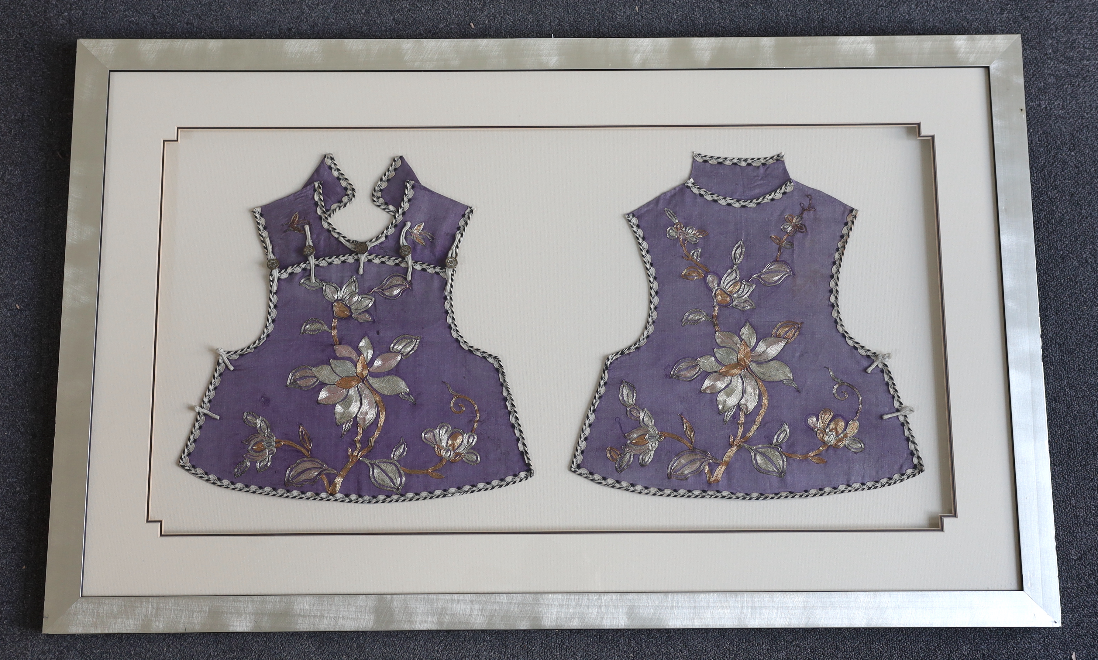 A late 19th century Chinese child’s purple silk and multi-coloured metal embroidered tabbard, front and back panels split and double mounted in one frame, 33cm wide, 37cm high